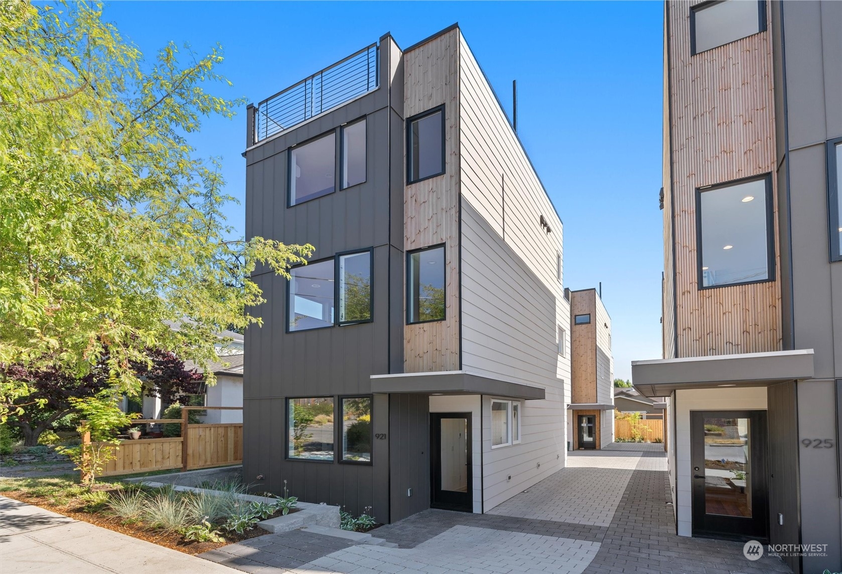 Modern townhomes with wood accents and rooftop deck railings along a paved walkway.