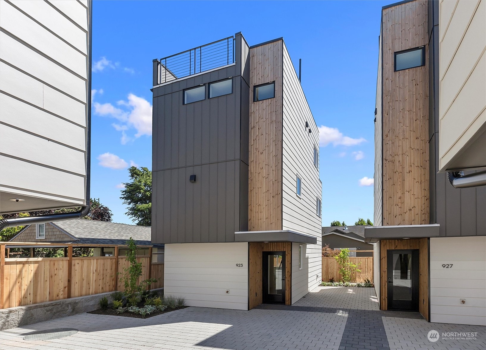 Modern townhomes with rooftop decks and wood-and-metal siding, facing a paved courtyard.