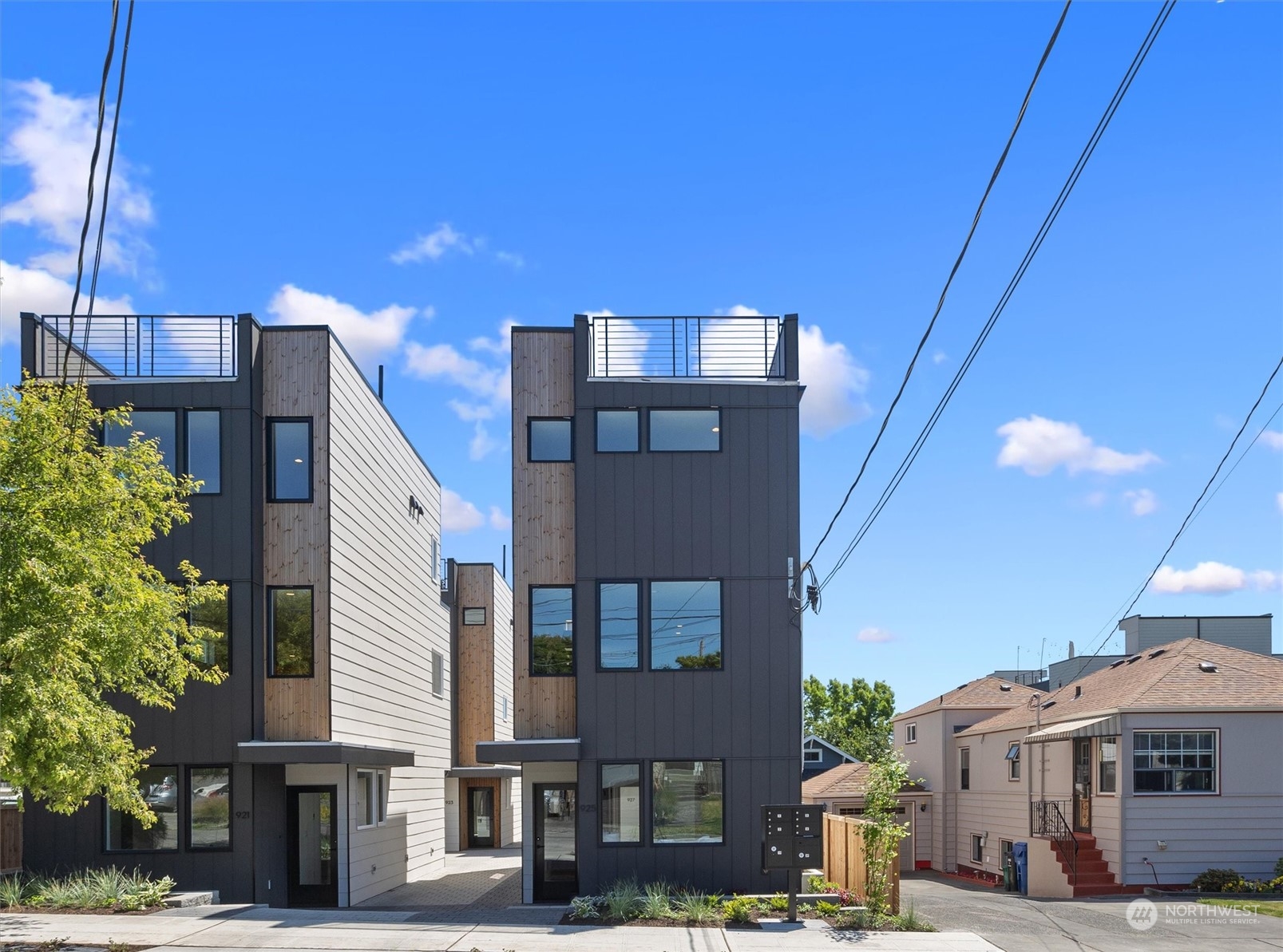 Modern townhomes with dark siding, wood accents, and rooftop decks along a residential street.
