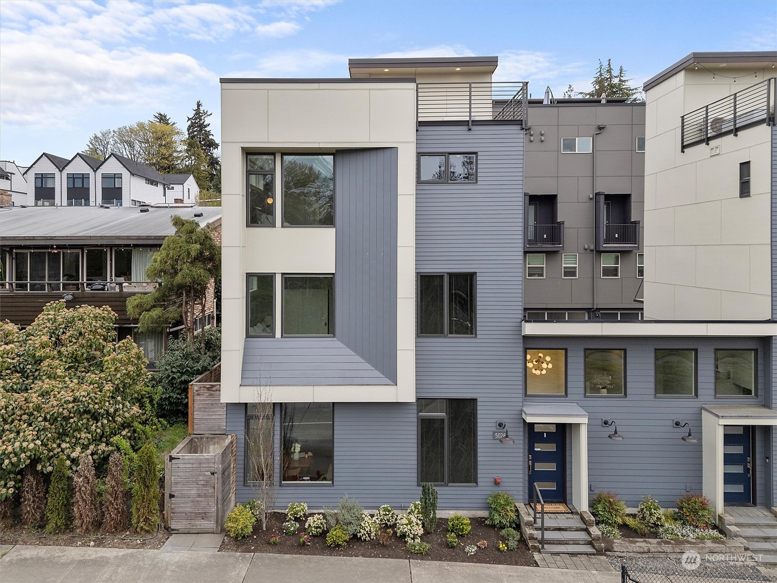 Modern blue-gray townhouse with a rooftop deck, geometric facade, and landscaped front entry.