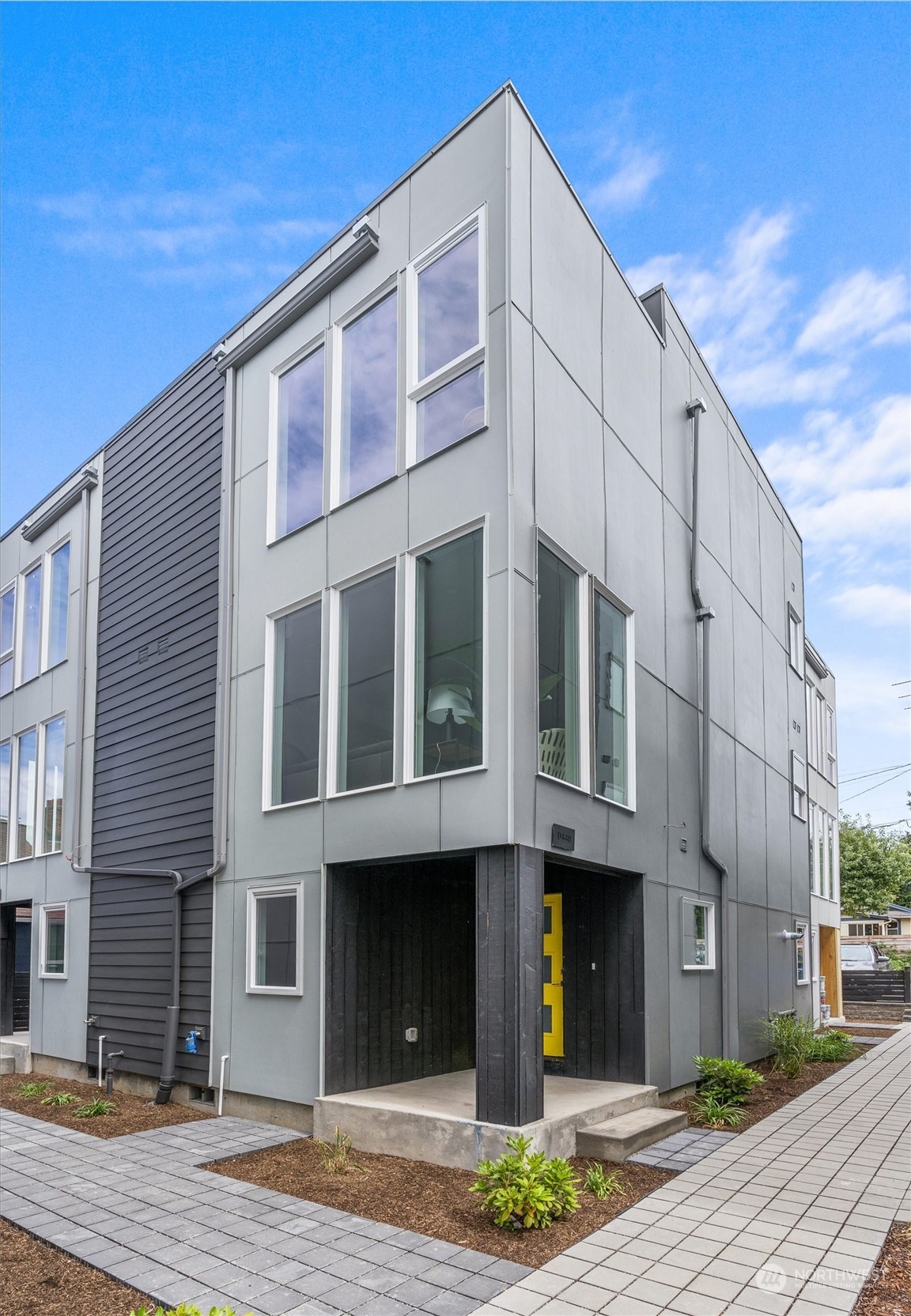 Modern gray townhome with tall windows, dark siding, and a bright yellow front door.
