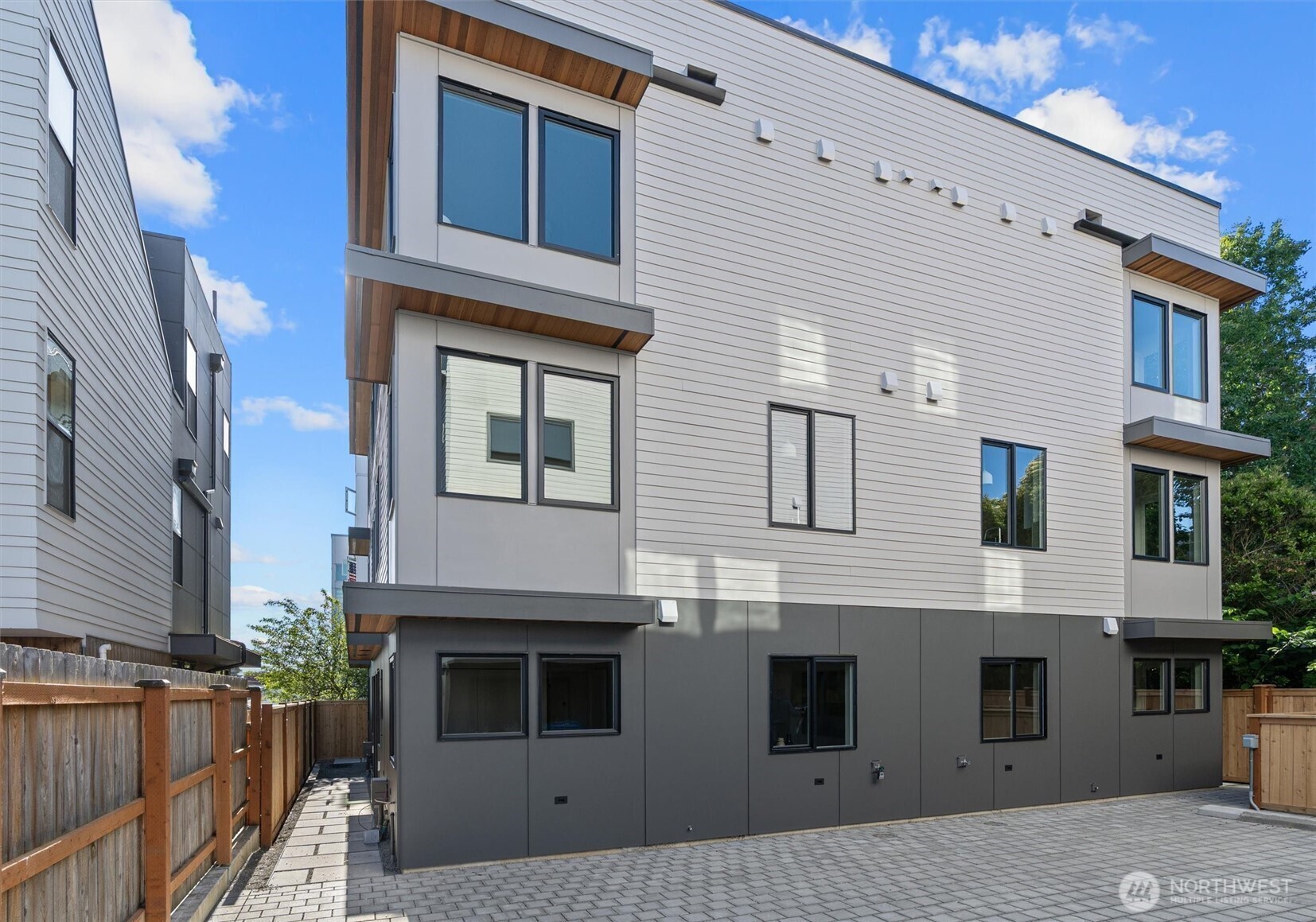 Modern multi-story home with white siding, wood soffits, and a paved fenced courtyard.