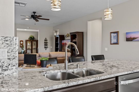 Kitchen island with granite countertop, double sink, pendant lights, and an open view into the living area.