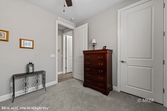 Bedroom with gray carpet, a dark wood dresser, ceiling fan, and open doorway.