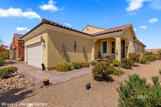 Tan stucco home with a white two-car garage, red tile roof, and desert landscaping.