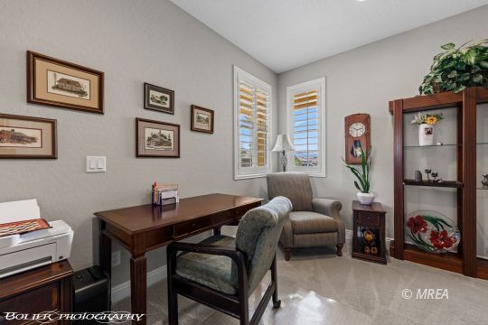 Furnished home office with a dark wood desk, shuttered windows, and framed artwork.