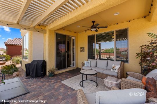 Covered patio with pergola, ceiling fan, and cushioned wicker seating beside sliding glass doors.