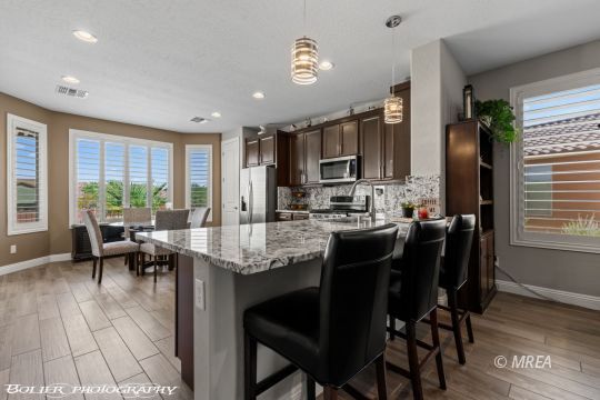 Kitchen with a granite island, black bar stools, dark cabinets, and a dining area beside large windows.