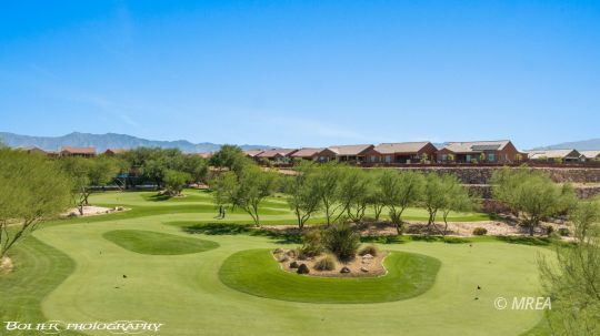 Golf course with a winding green, desert landscaping, and homes along the distant ridge.
