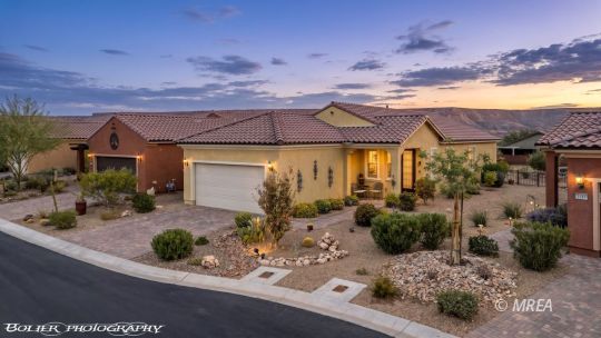 Single-story stucco home with a tile roof, attached garage, and desert landscaping at sunset.