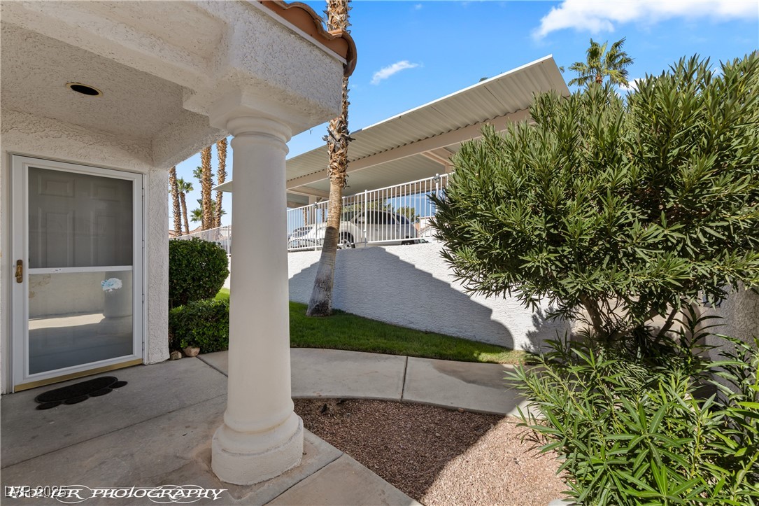 Covered entry patio with a white column, screened door, desert landscaping, and palm trees.