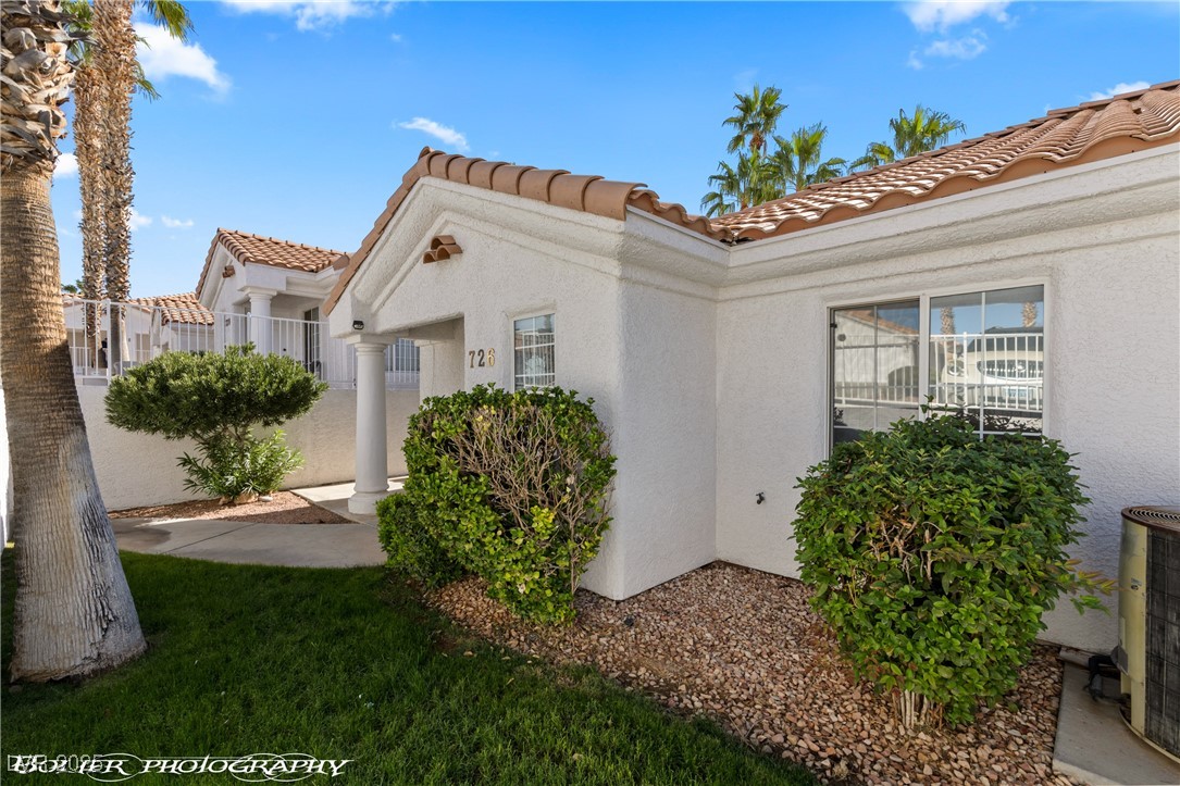 Home exterior with white stucco, tiled roof, covered entry, trimmed shrubs, and palm trees.