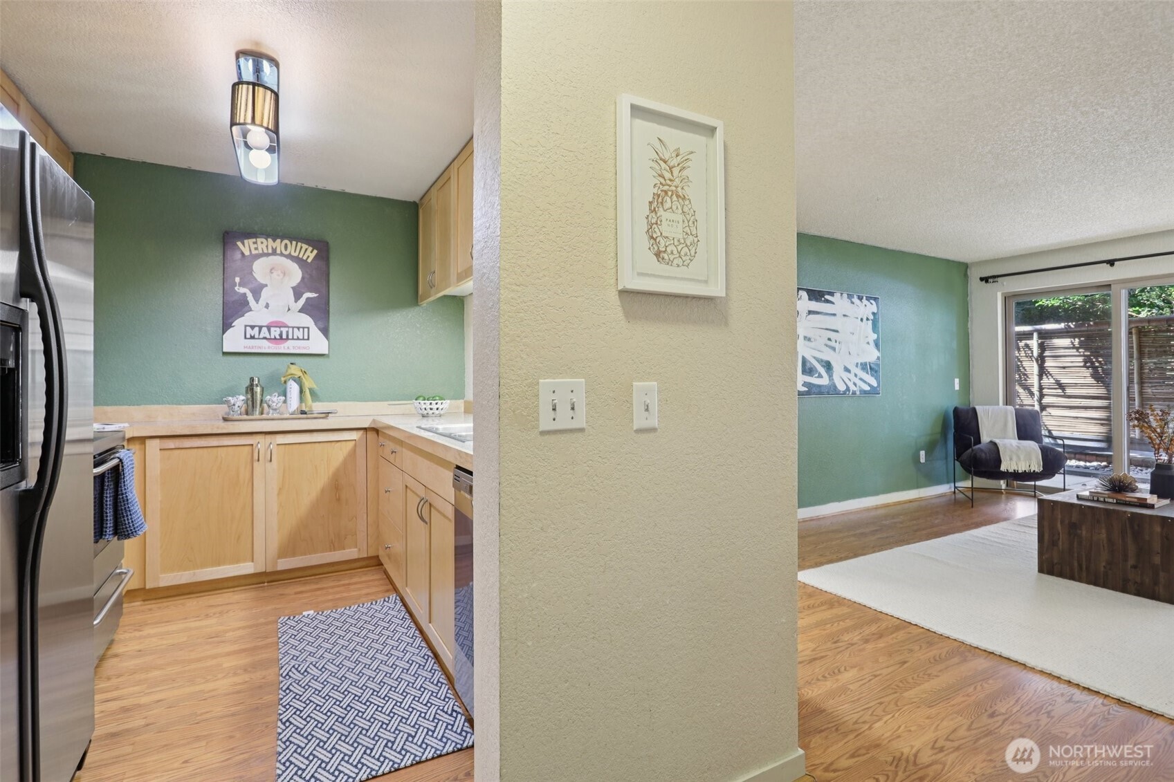 Kitchen opening into a living area with green walls, light wood cabinets, and sliding glass doors.