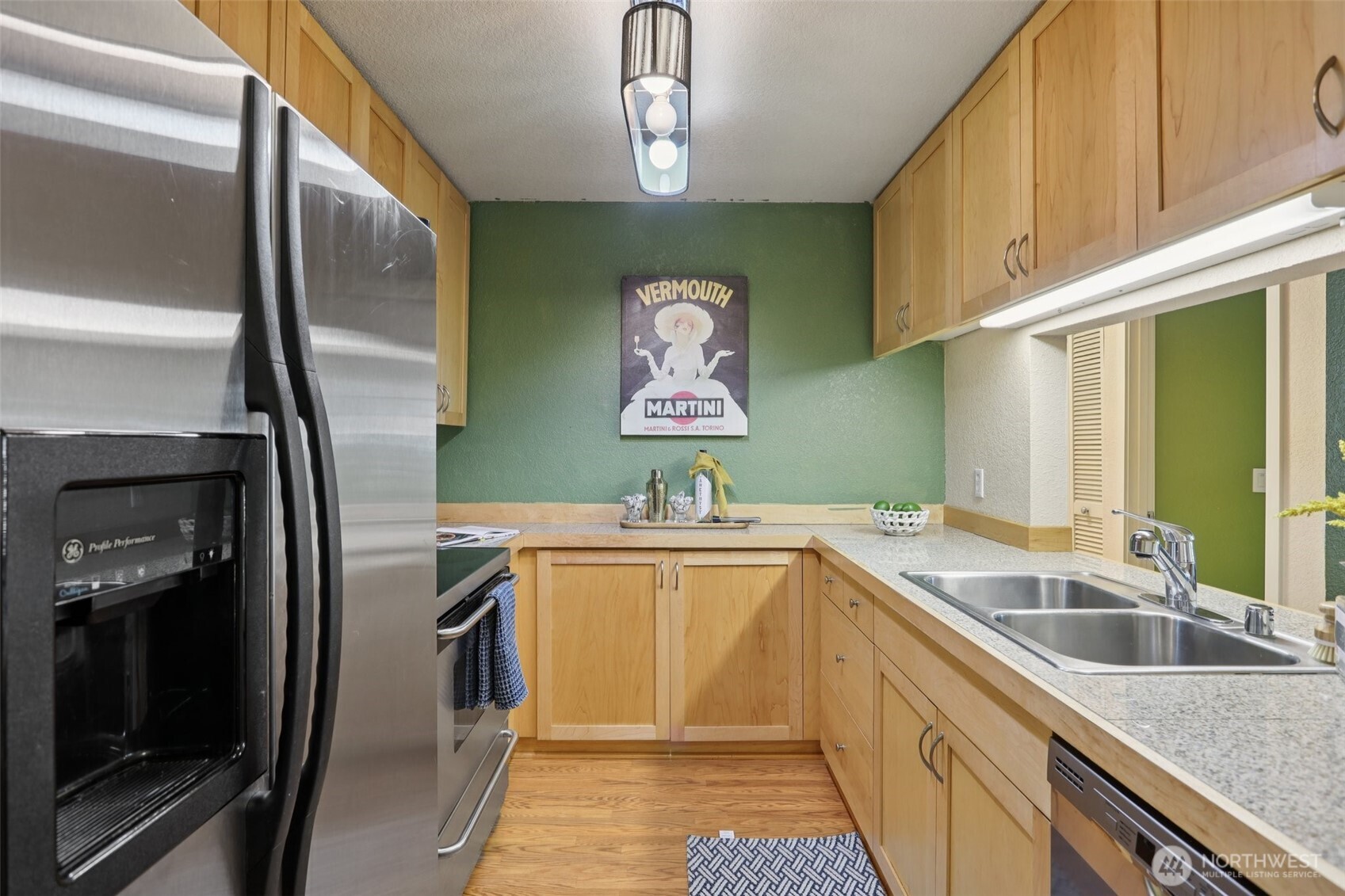 Galley kitchen with light wood cabinets, stainless steel appliances, granite counters, and green walls.