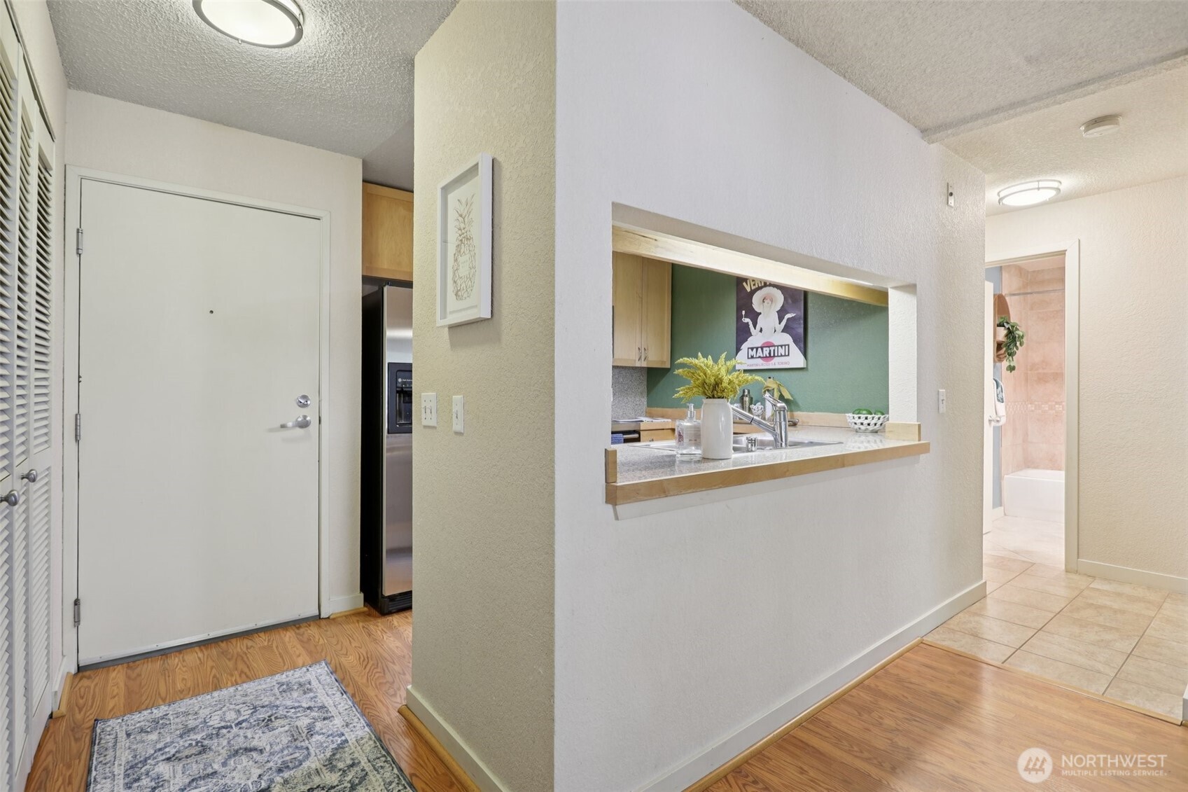 Condo entryway with a kitchen pass-through and a tiled hallway leading to the bathroom.