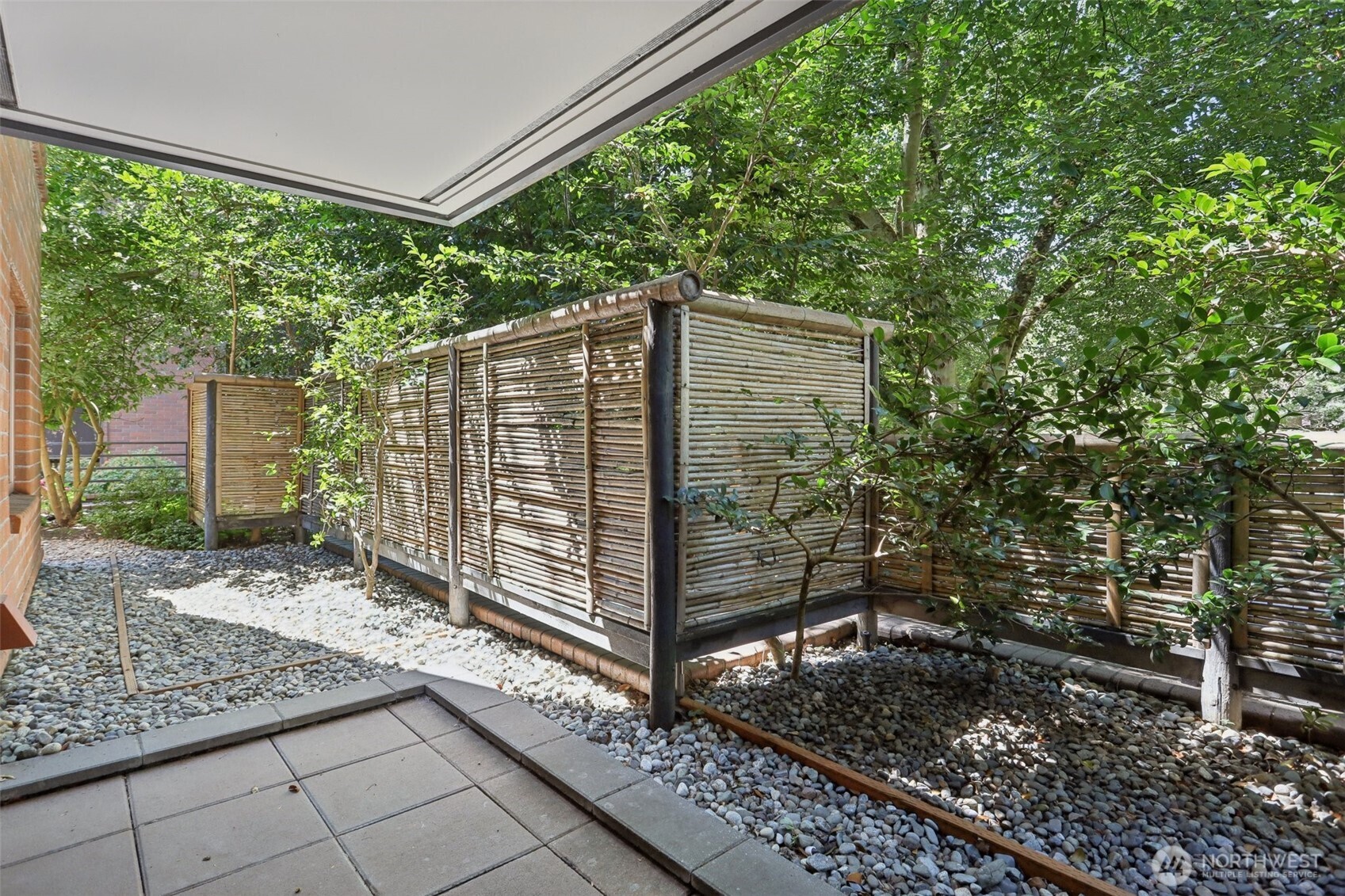 Patio with bamboo privacy screens, leafy trees, and river-rock landscaping.