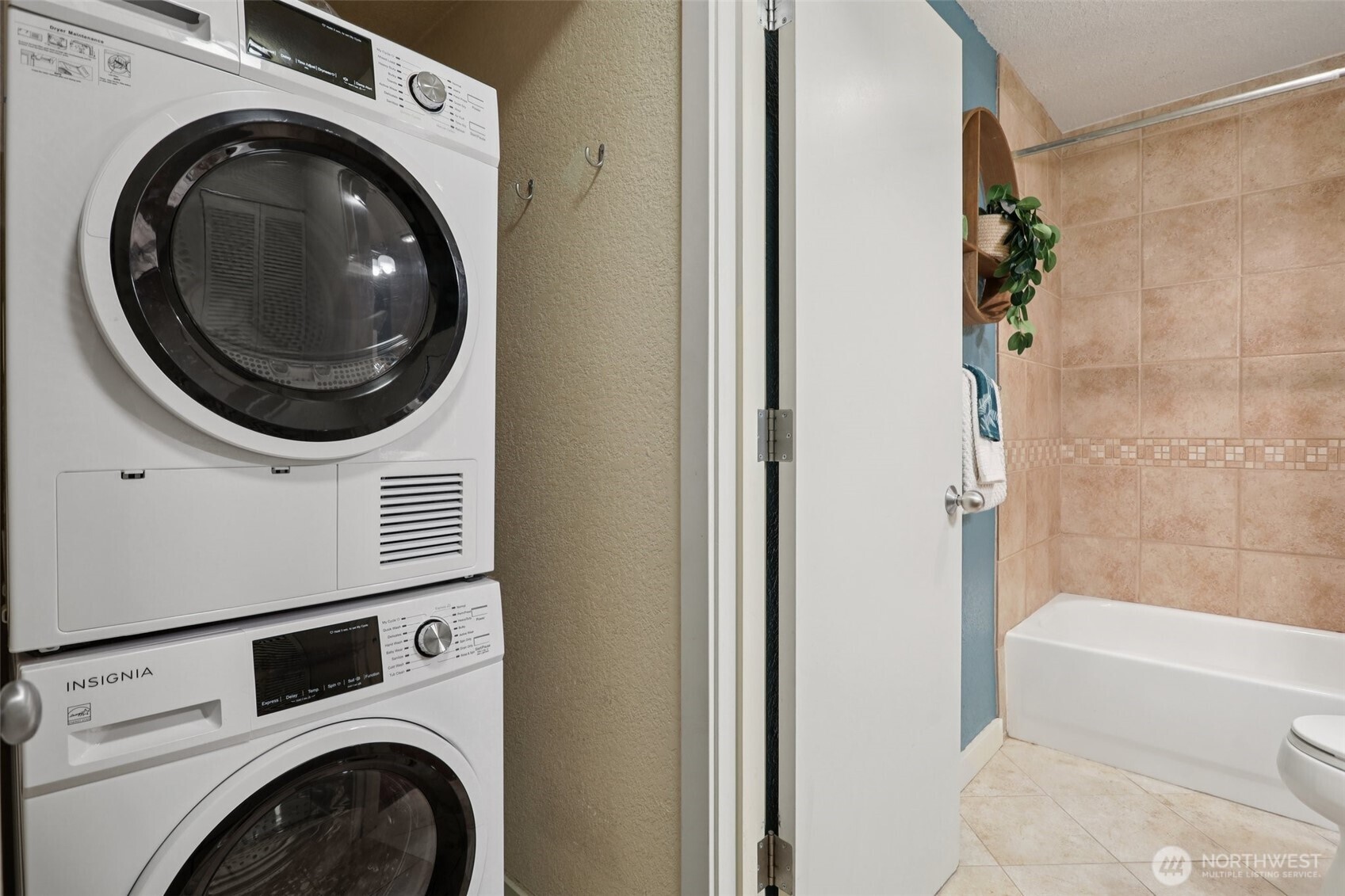 Stacked washer and dryer beside a beige-tiled bathtub and shower.