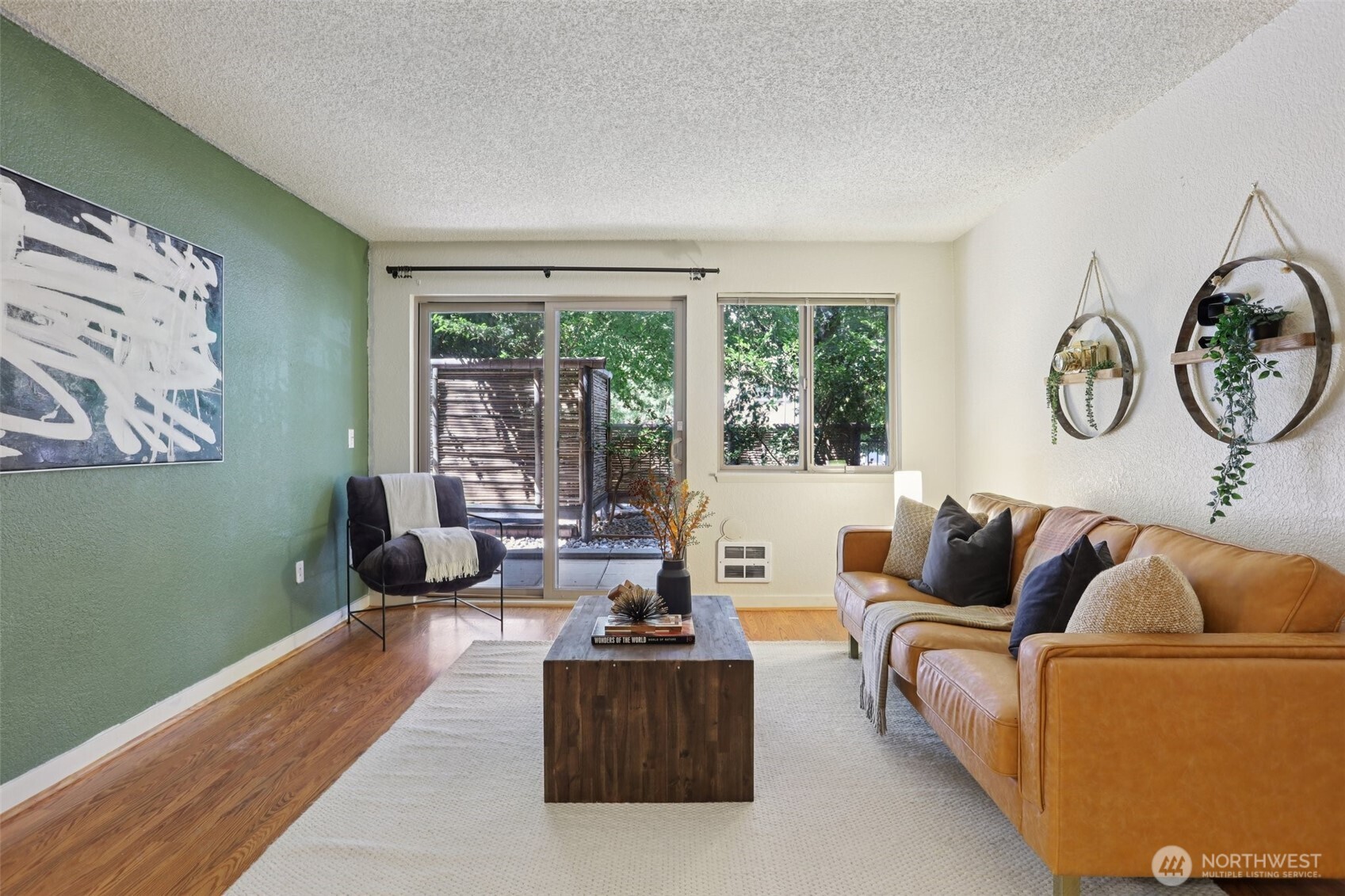 Living room with a green accent wall, leather sofa, and sliding doors to a leafy patio.
