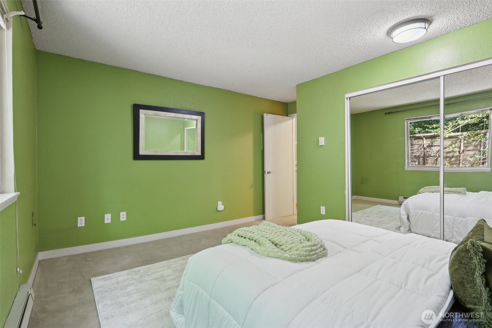 Bedroom with bright green walls, a white bed, and mirrored closet doors.