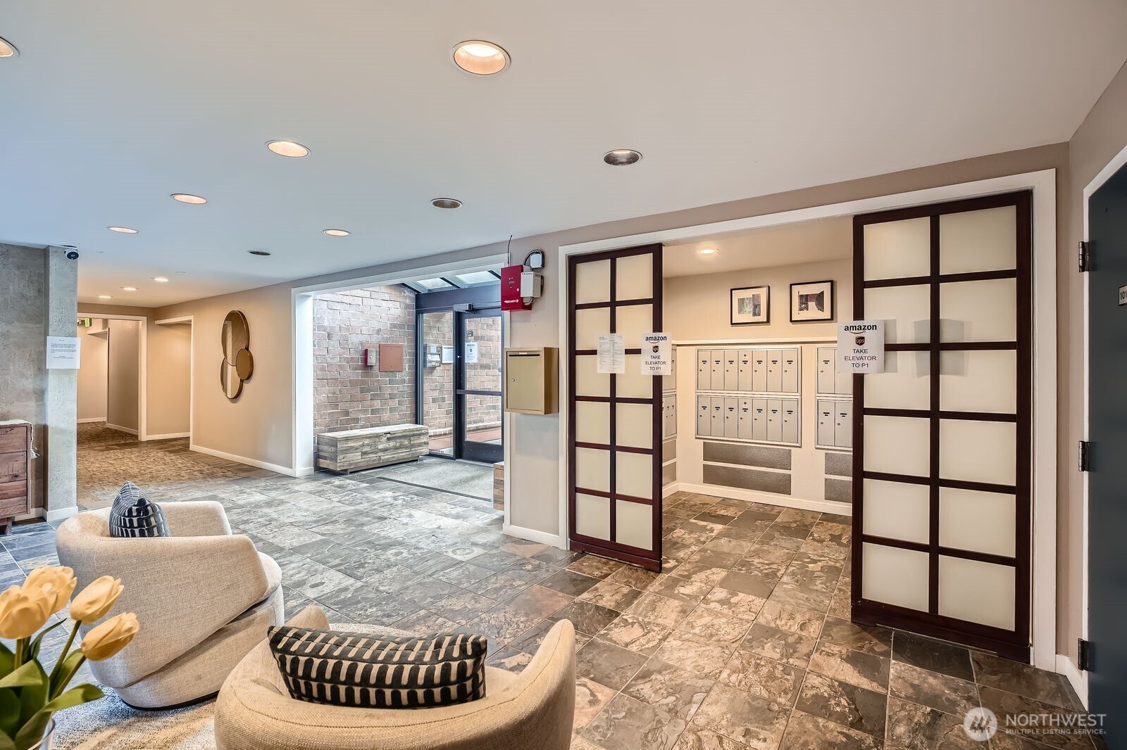 Condominium lobby with a tiled floor, lounge seating, glass entrance, and mailroom.