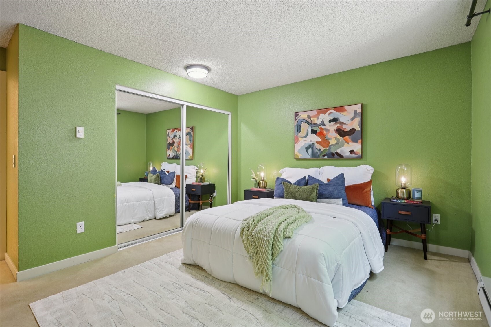 Bedroom with green walls, a white bed, mirrored closet doors, and abstract art.