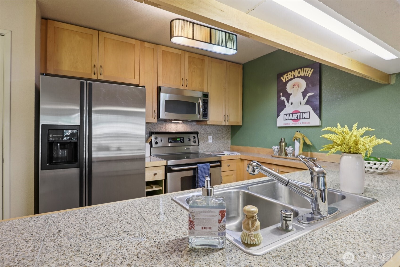 Kitchen with light wood cabinets, stainless steel appliances, and a foreground island sink.