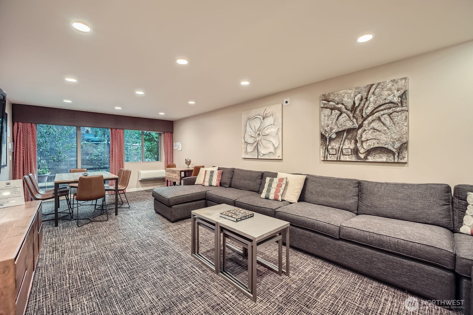 Furnished living and dining area with a large gray sectional and broad windows.