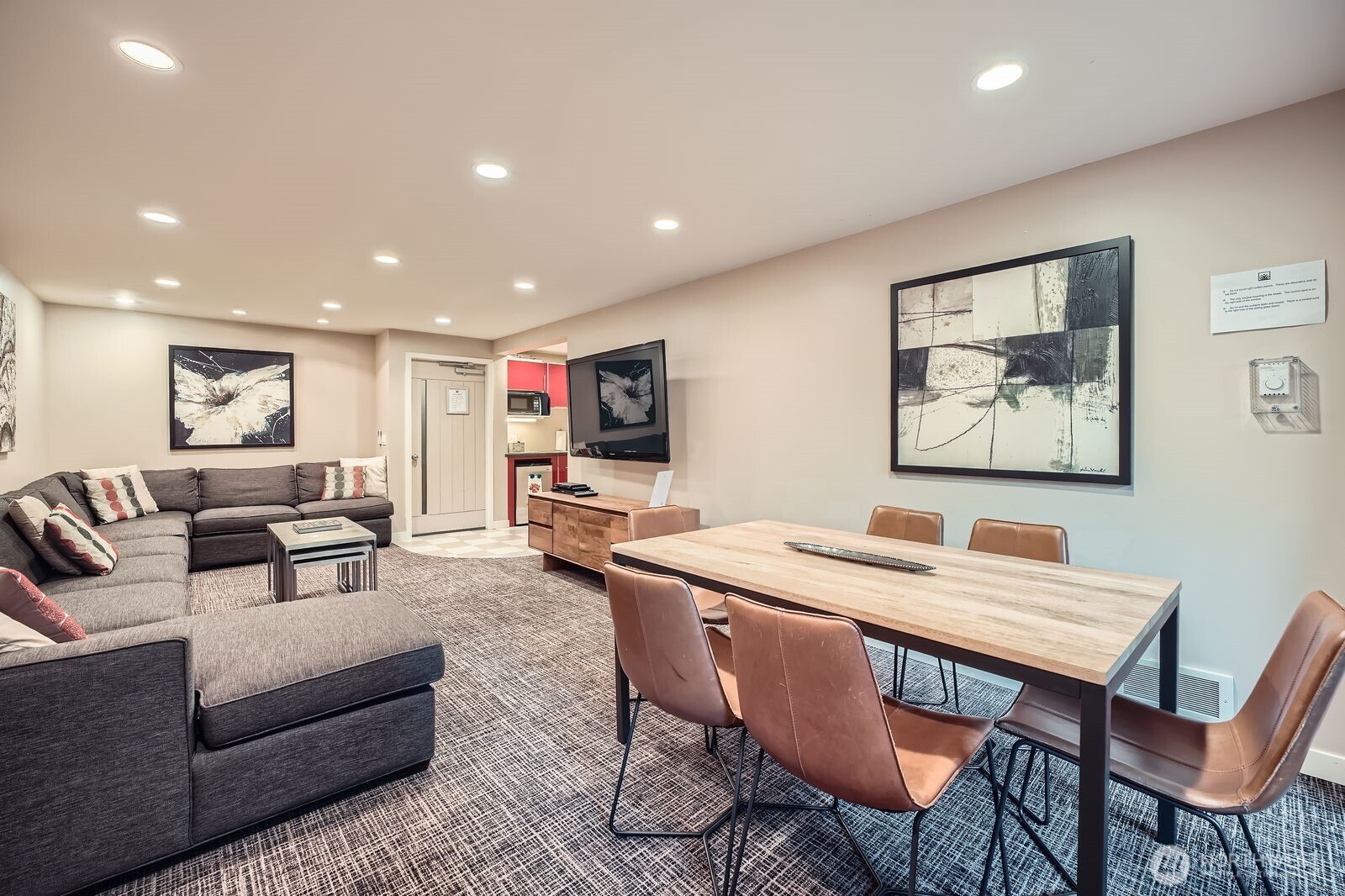 Living and dining area with a gray sectional, long wood table, and kitchenette.