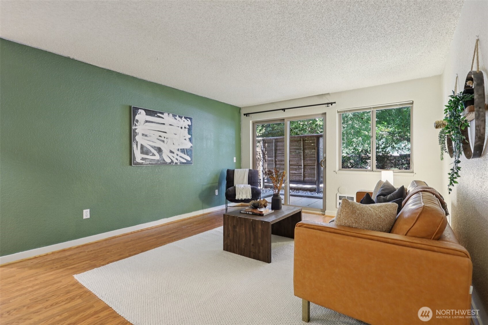 Staged living room with a green accent wall, tan leather sofa, hardwood floors, and doors to a private patio.