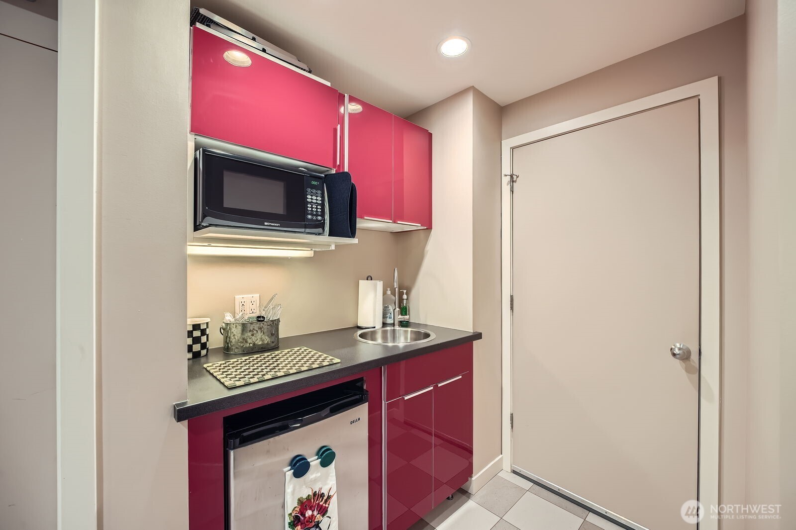 Compact kitchen with glossy magenta cabinets, a microwave, sink, and under-counter refrigerator.