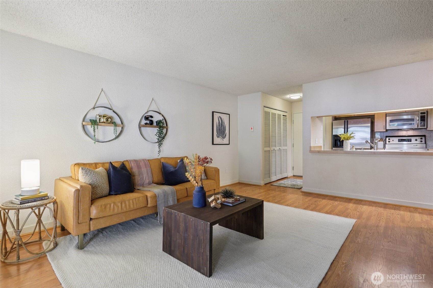 Living room with a tan leather sofa, dark coffee table, and hardwood floors beside the kitchen.