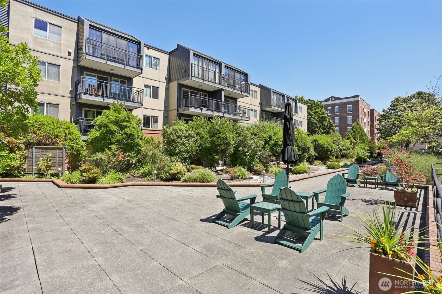 Apartment courtyard patio with teal Adirondack chairs, landscaped garden beds, and balconies.