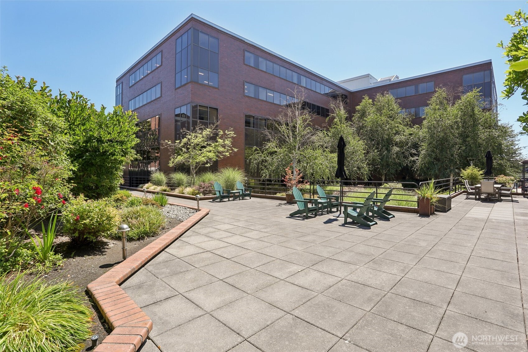 Modern brick building beside a landscaped patio with green lounge chairs and outdoor dining furniture.