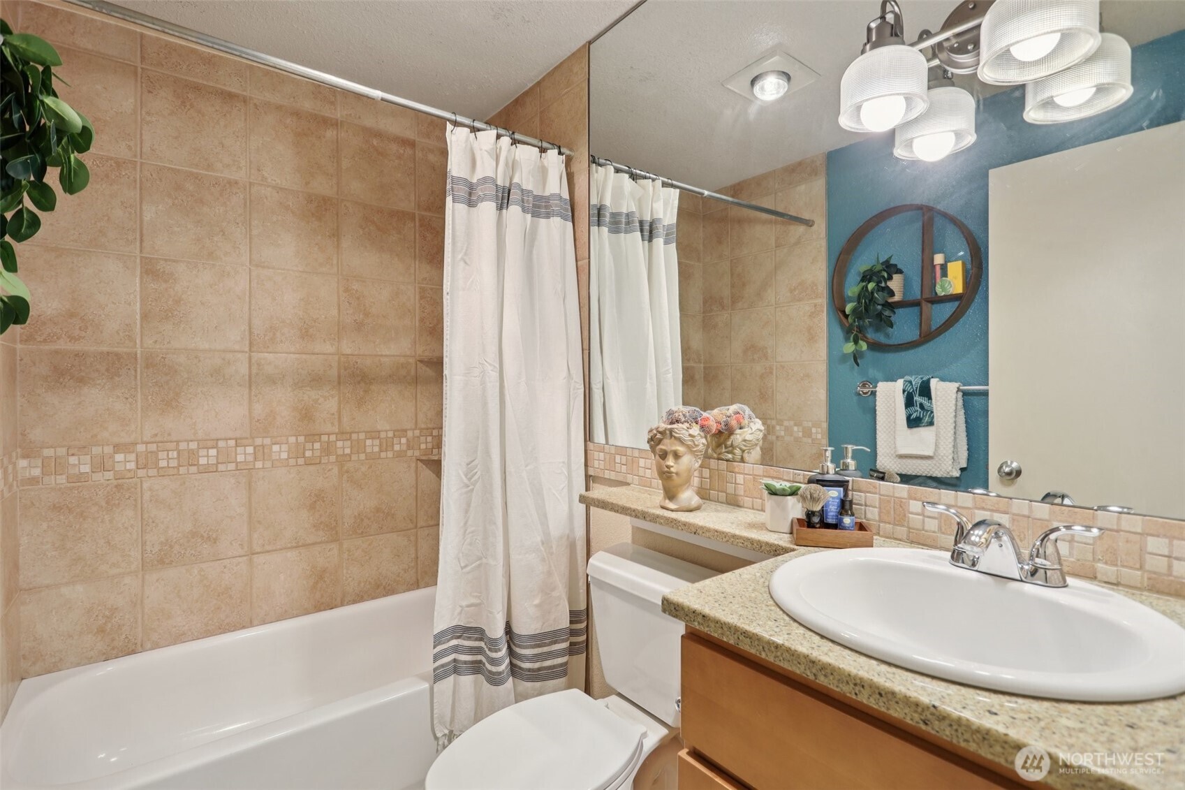 Bathroom with tan tile, a striped shower curtain, and a granite vanity.