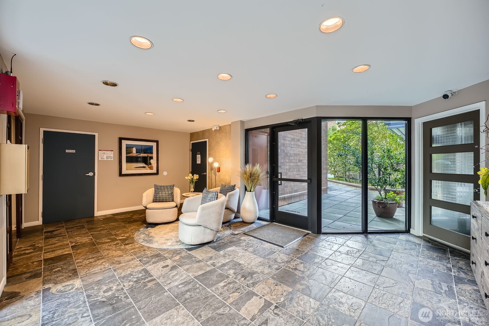 Lobby with stone-tile floors, a seating area, and glass doors opening to a planted courtyard.