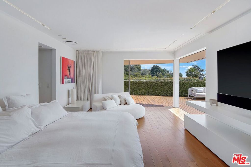 Bright living room with white sofas, wood floors, and sliding doors opening onto a deck.