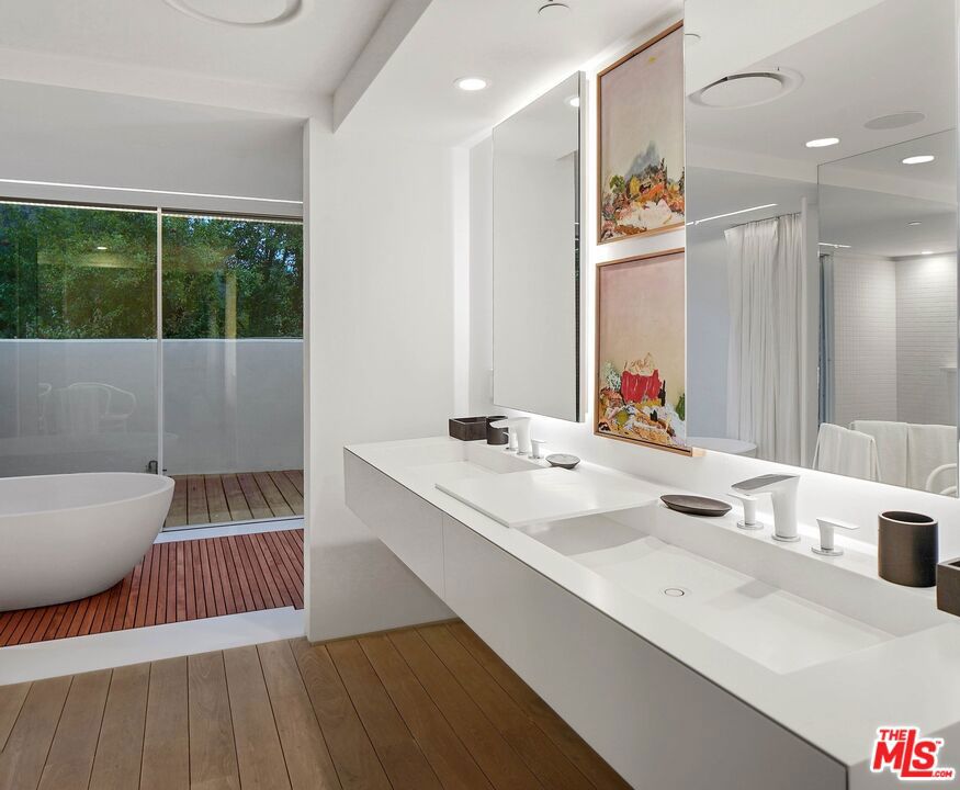 Modern bathroom with a long double vanity and freestanding tub beside glass doors to a wood deck.