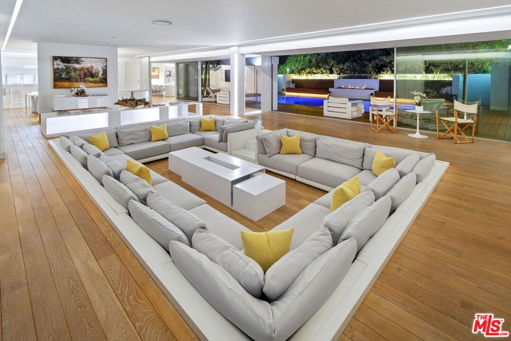 Modern living room with a large sectional, warm wood floors, and glass doors opening to a pool patio.