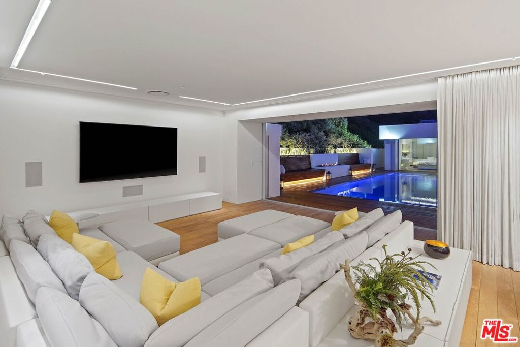 Modern living room with a white sectional and wide doors overlooking an illuminated pool.