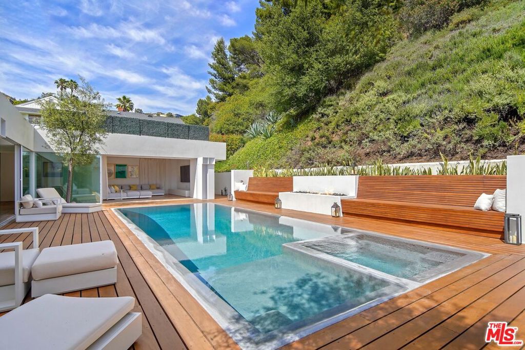 Swimming pool and raised spa beside a modern white house, with a wood deck and hillside landscaping.