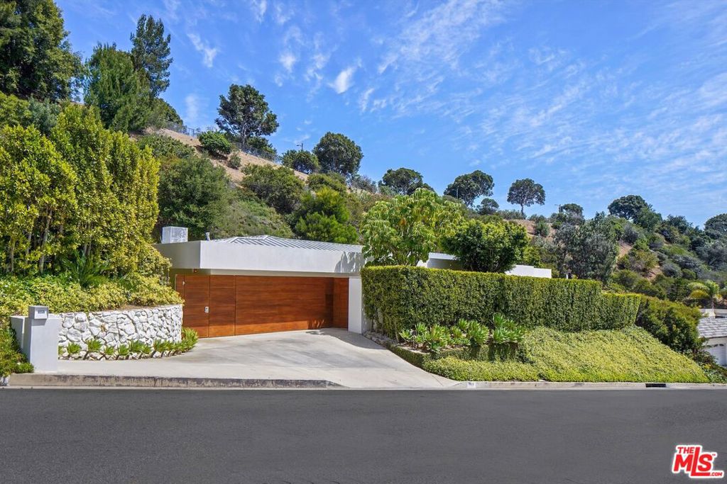 Modern hillside home with a broad wood-paneled garage door, landscaped driveway, and stone retaining wall.