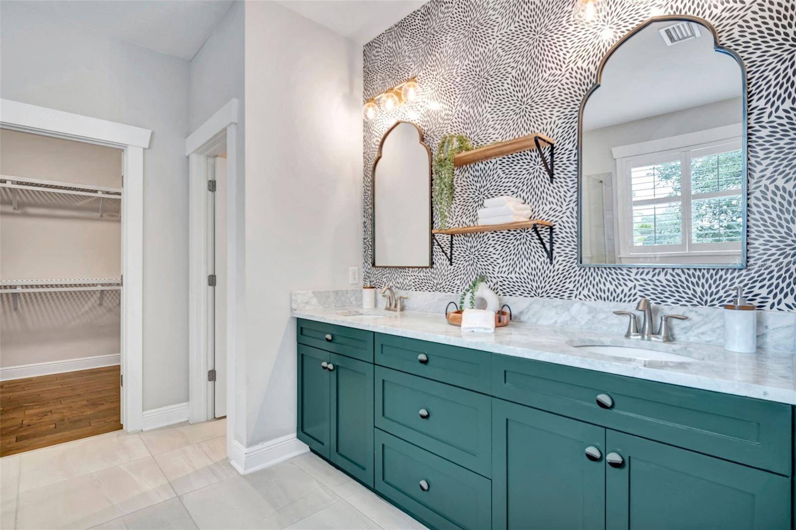 Bathroom with a teal double vanity, marble countertop, patterned accent wall, and arched mirrors.
