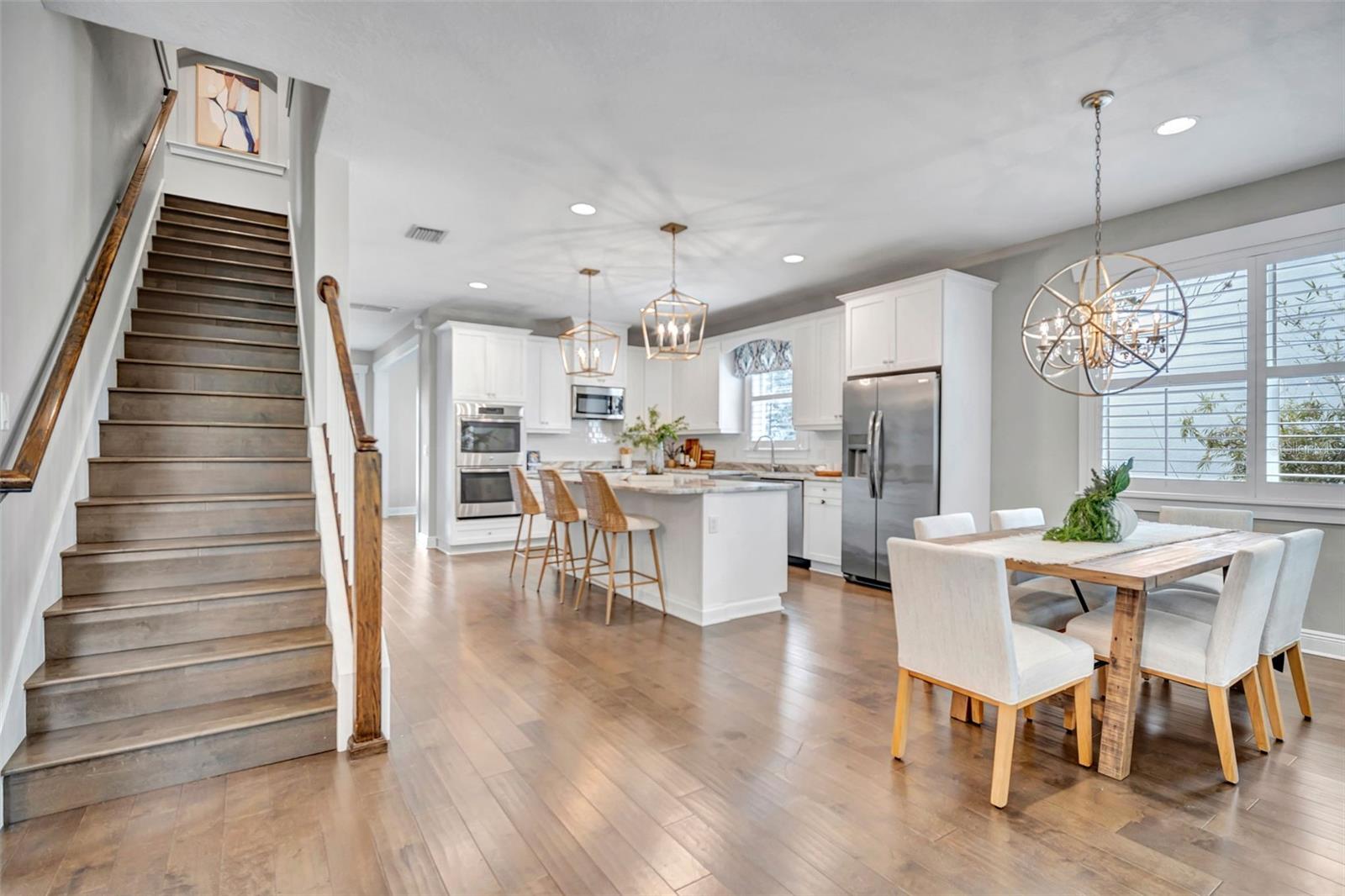 Open-plan kitchen and dining area with a large island, stainless appliances, and a staircase with wood handrails.