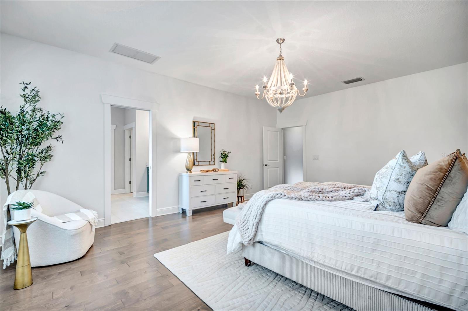 Bright bedroom with a large white bed, crystal chandelier, and wood floors.
