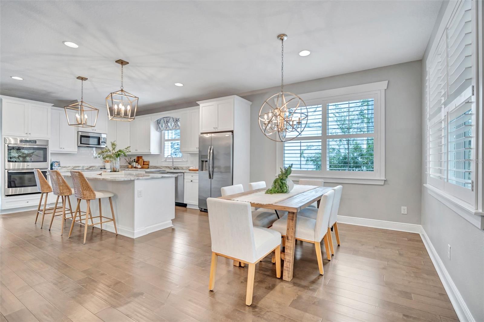 Open kitchen and dining area with a large island, woven bar stools, and plantation-shuttered windows.
