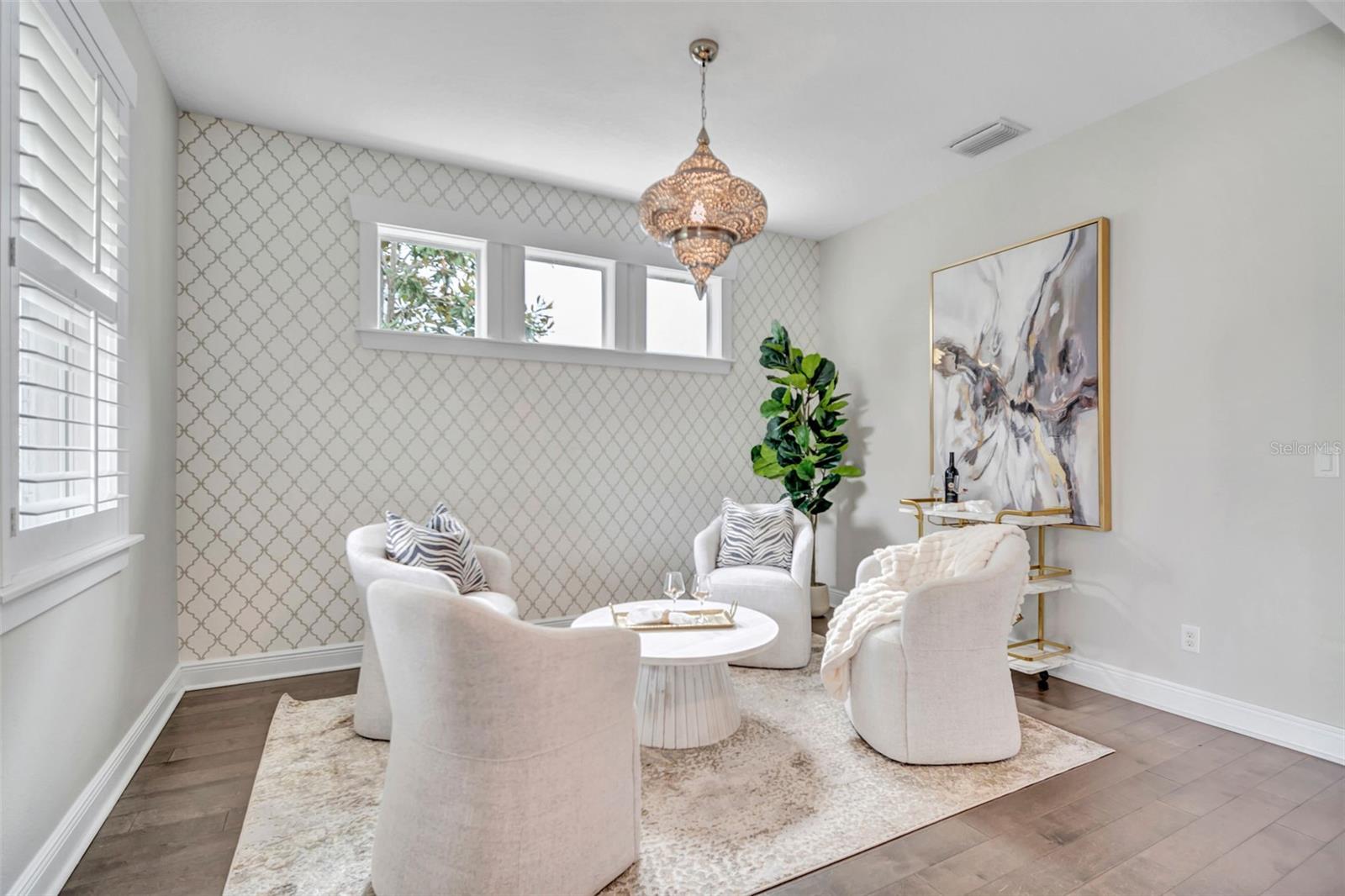 Staged sitting area with white chairs, patterned wallpaper, and a decorative pendant light.