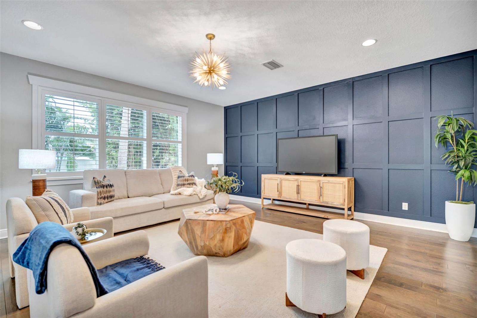 Living room with a navy paneled television wall, cream seating, and large shuttered windows.