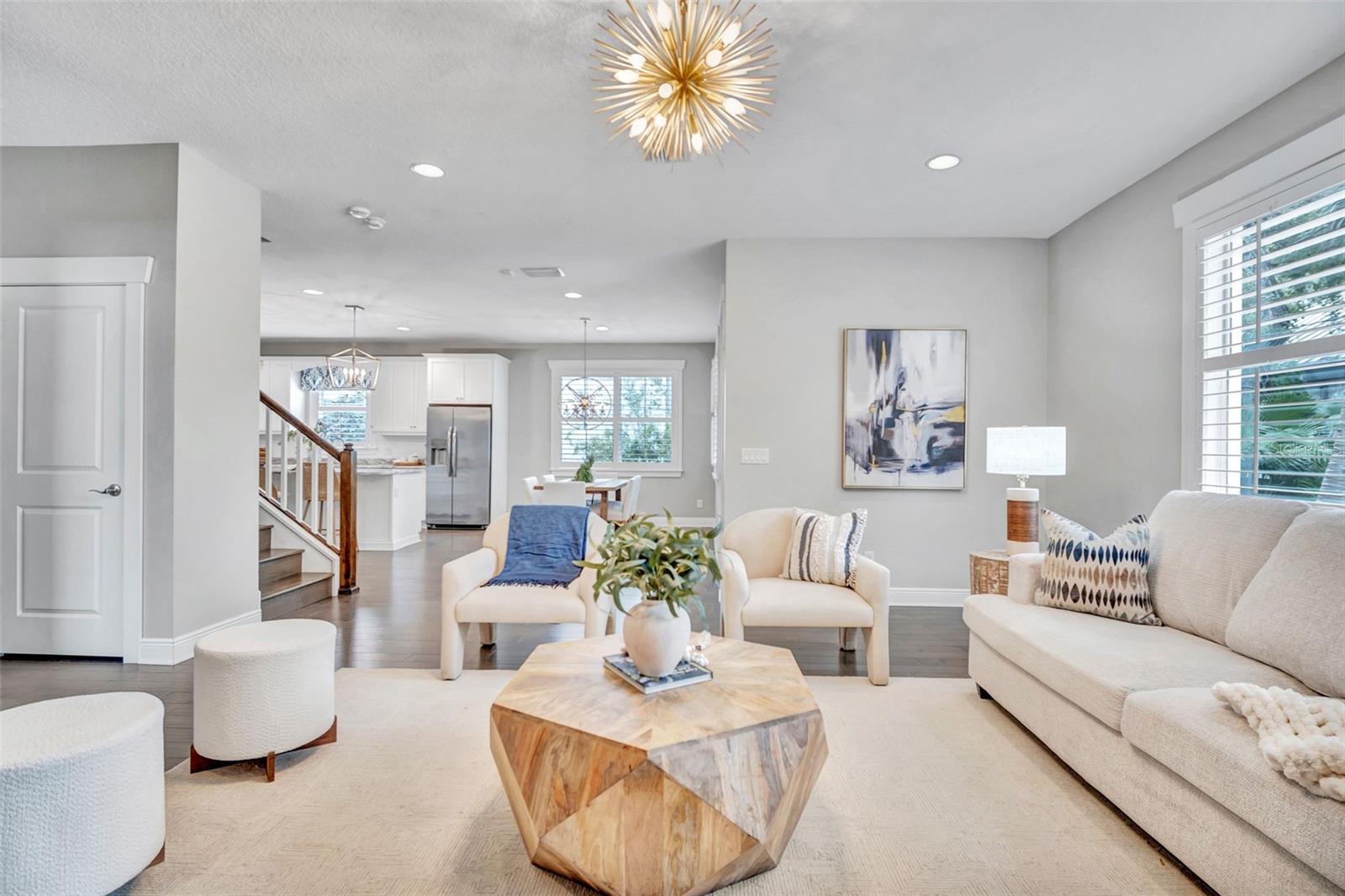 Staged living room with a geometric wood coffee table, cream seating, and an open kitchen.