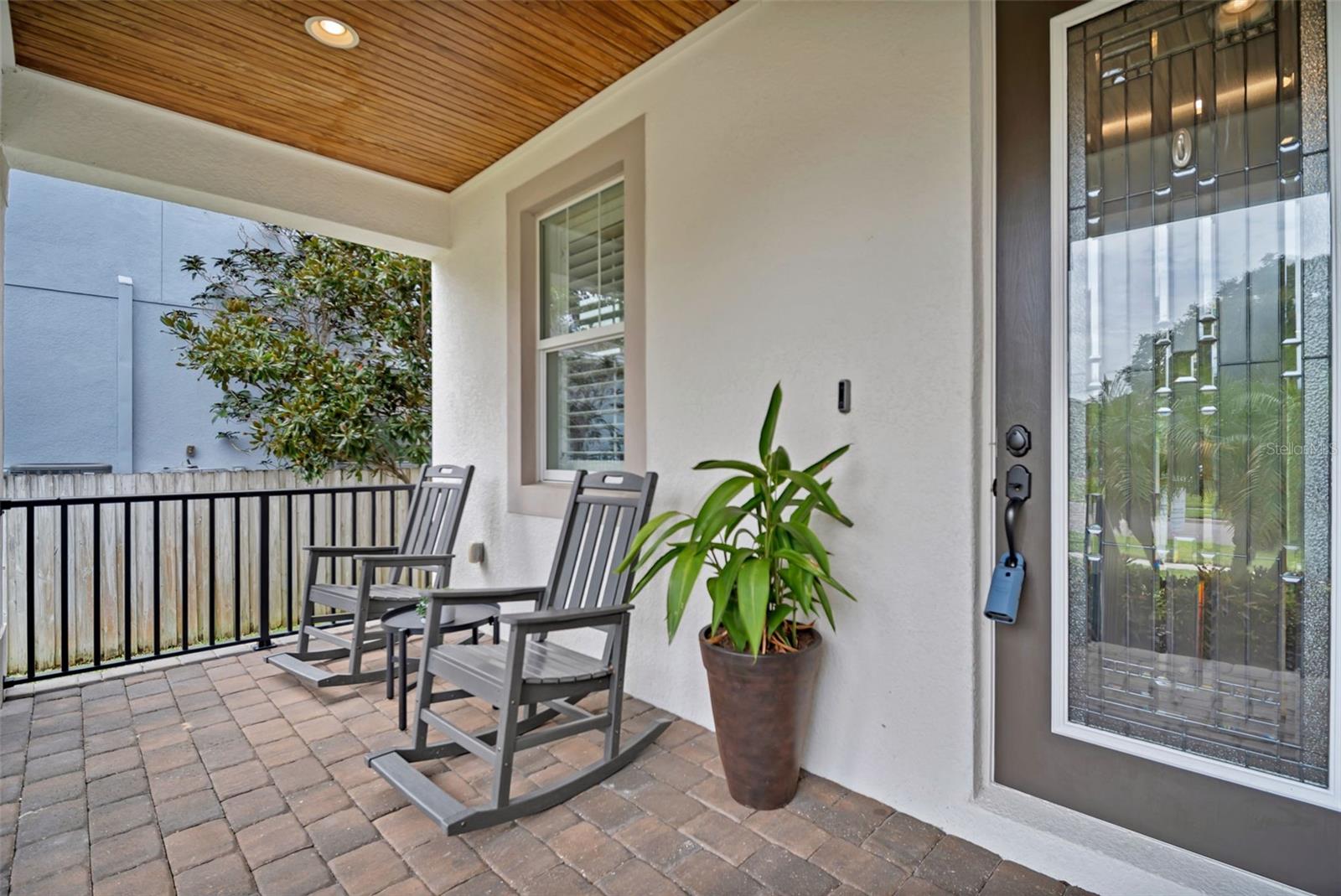 Covered front porch with brick pavers, two rocking chairs, and a wood-plank ceiling.