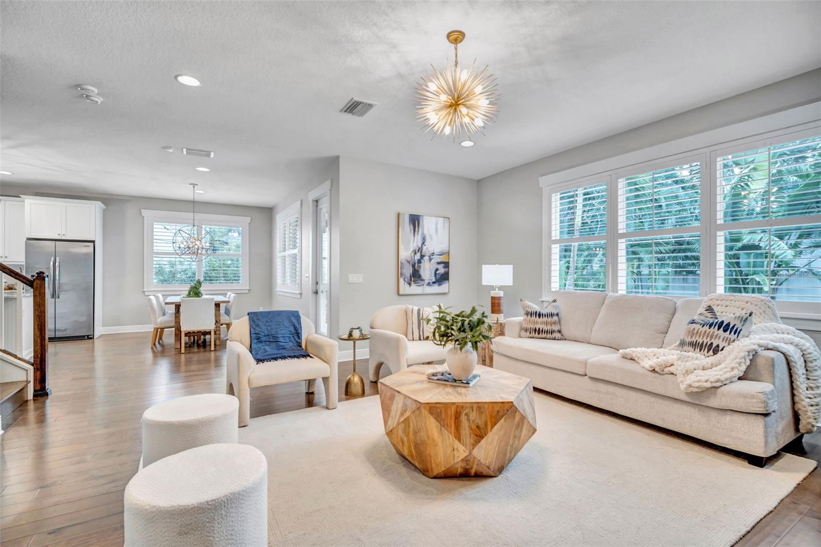 Furnished living room with a pale sectional, geometric wood coffee table, and large shuttered windows.